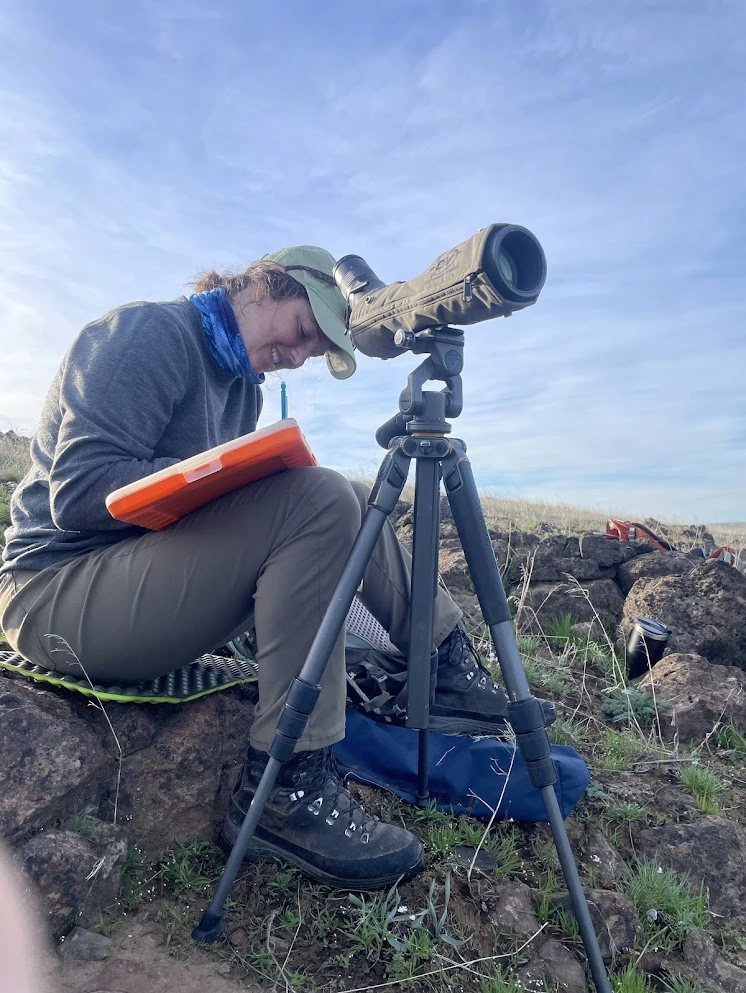 Emily Lowrimore makes notes in a notebook while sitting next to a tripod-mounted scope on the canyon rim above the John Day River.