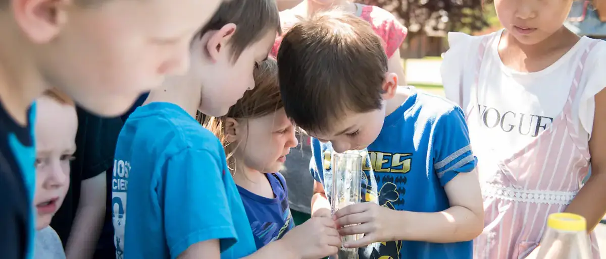 A group of kids looking down a glass beaker.