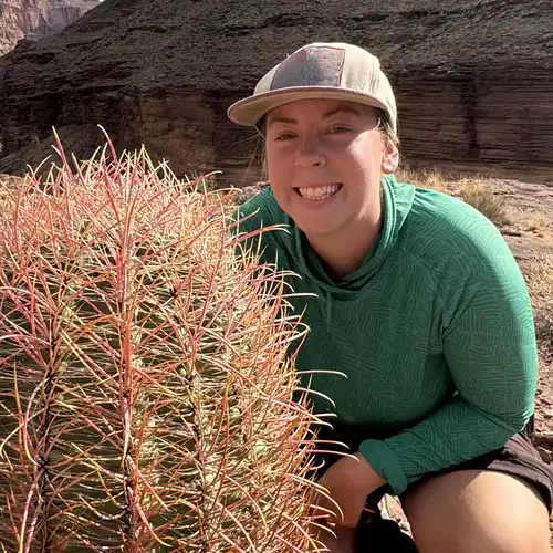 A women in the dessert squatting behind a cactus