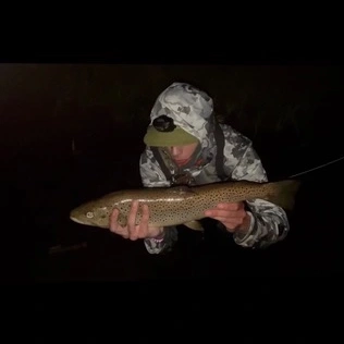 A student wearing camo holding a freshly-caught fish at night