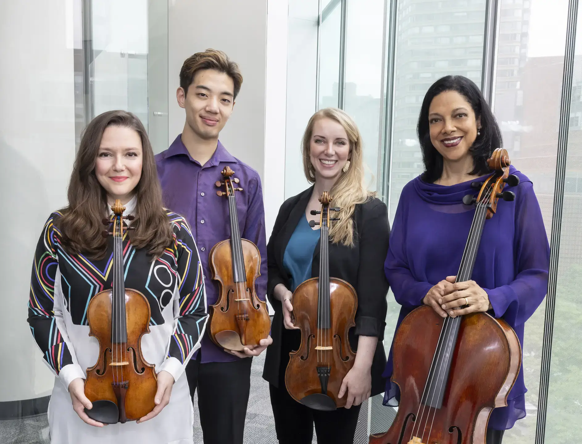 Four musicians holding string instruments stand together for a group photo.