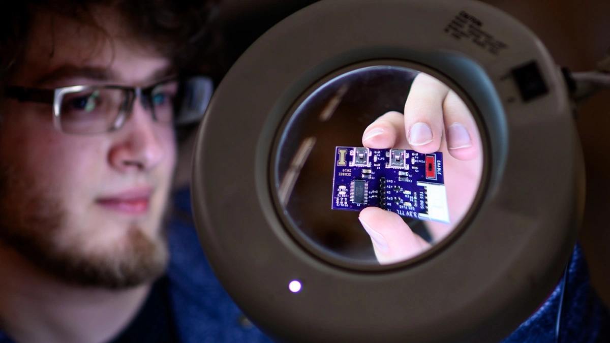 Students hold a microchip up to a magnifying glass.
