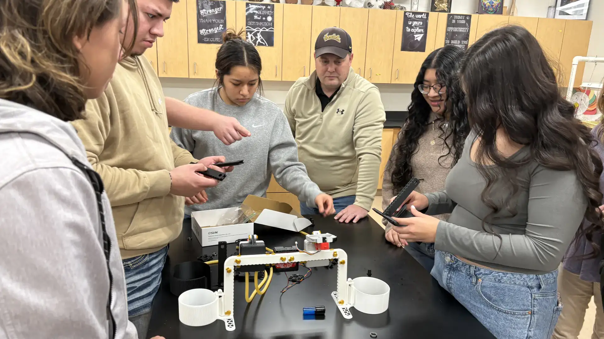High school students surround a table holding plastic parts and discussing how to assemble them into a robot.