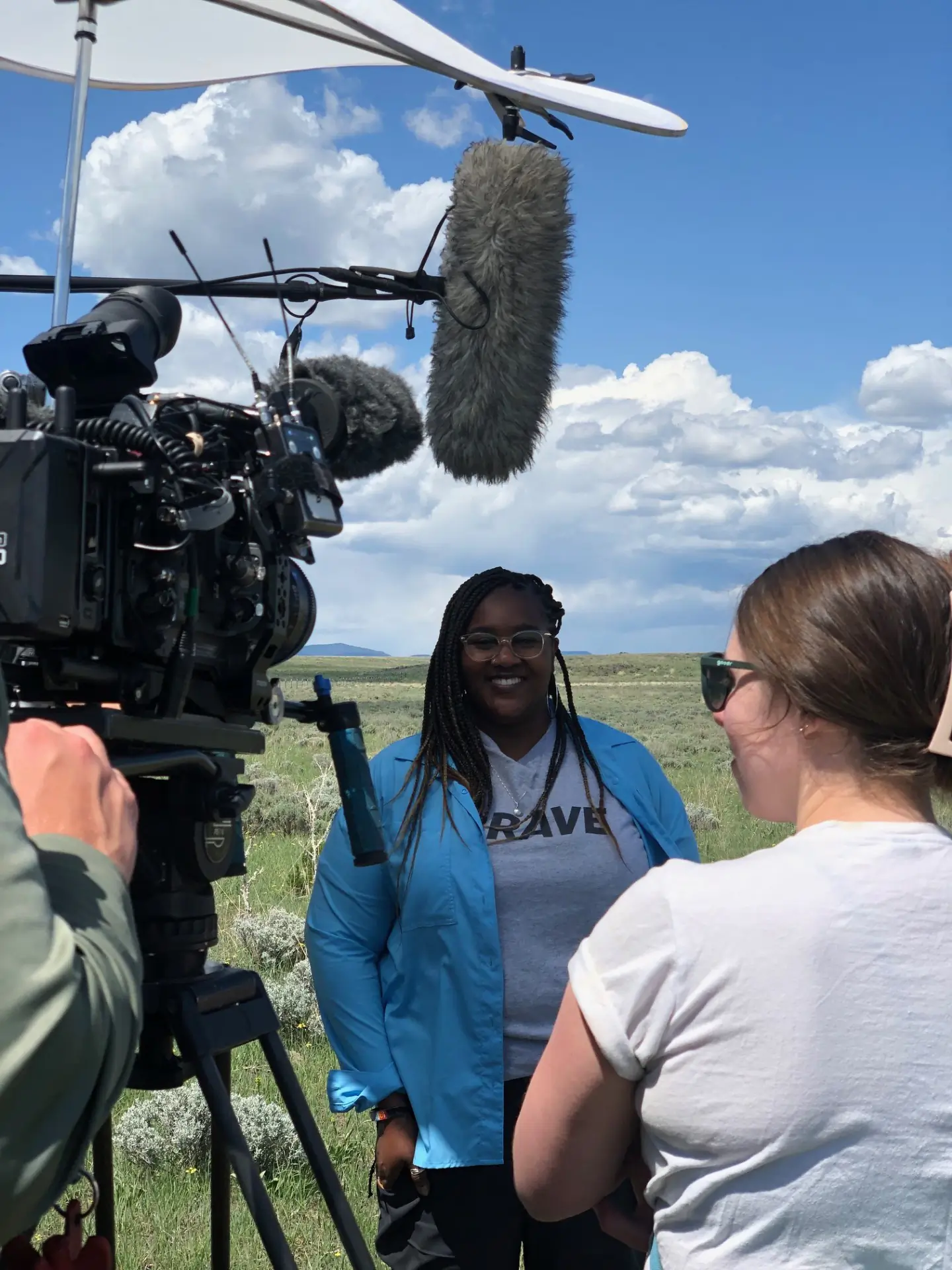 A woman smiles for a photo while being interviewed and surrounded by camera equipment.  