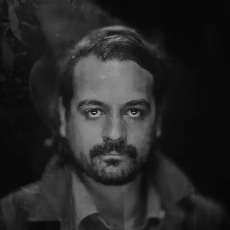 A monochrome portrait of a person with a solemn expression against a dark backdrop.