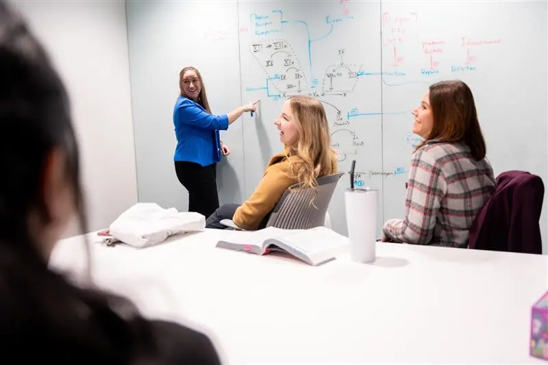 Four girls laughing and studying at a whiteboard.