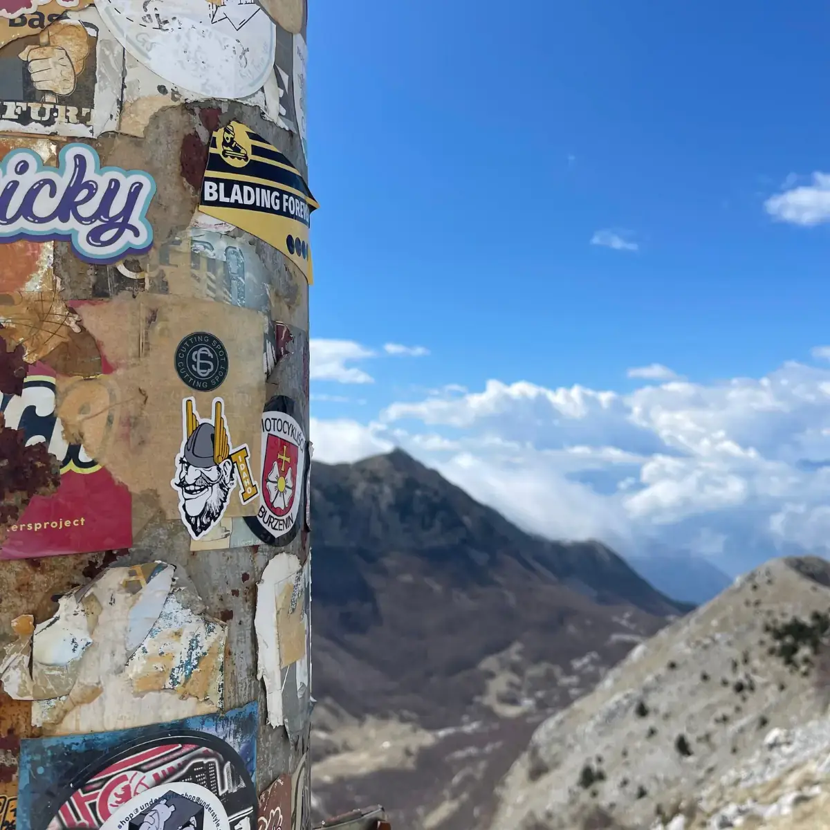 Stickers on a pole with mountains in the background.