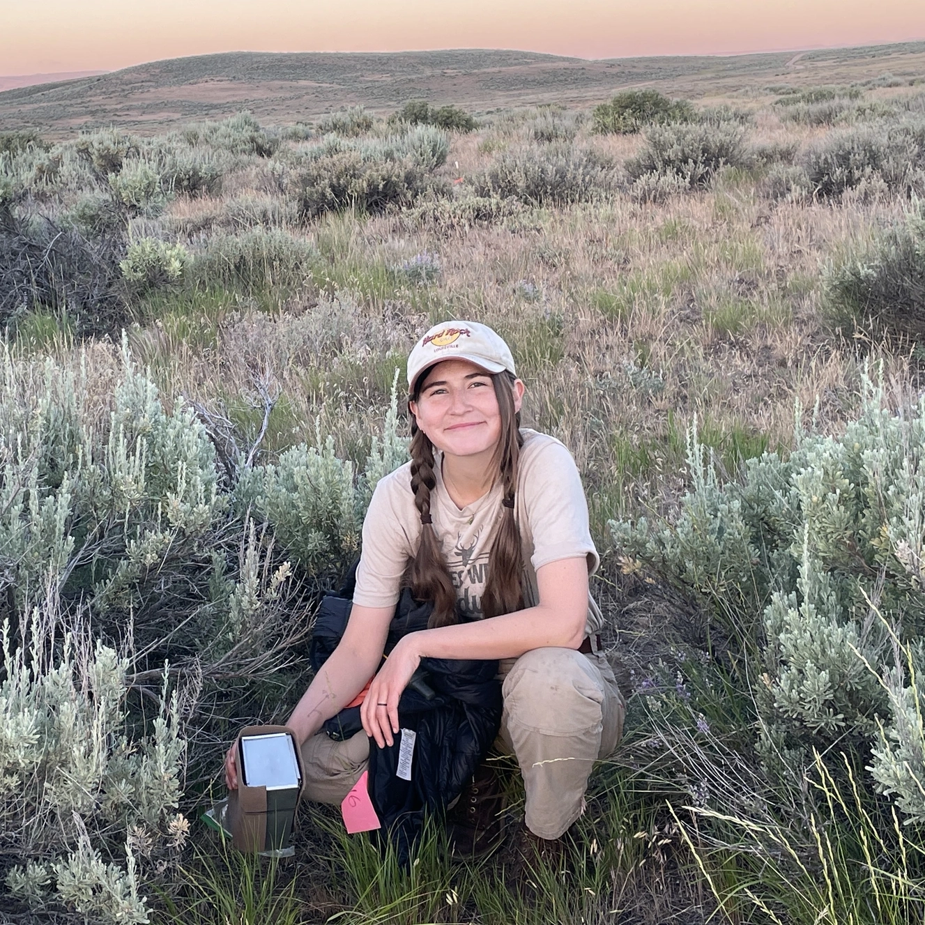 A woman out in the sage brush shows one of the metal traps she uses for capturing small mammals