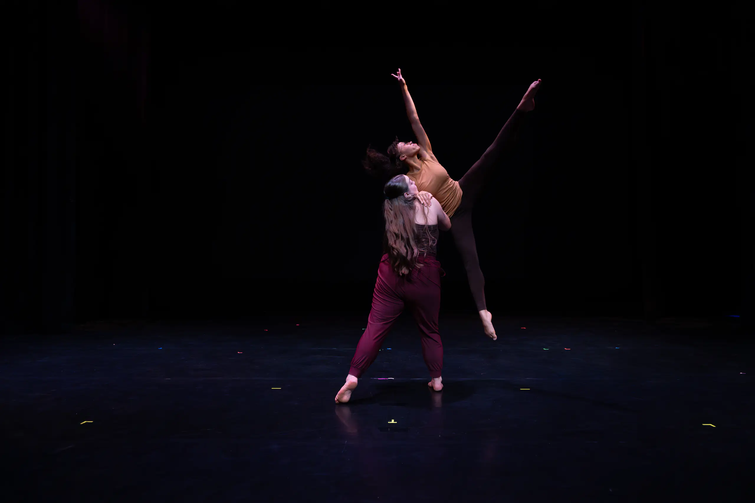 Two students dance on a dark stage
