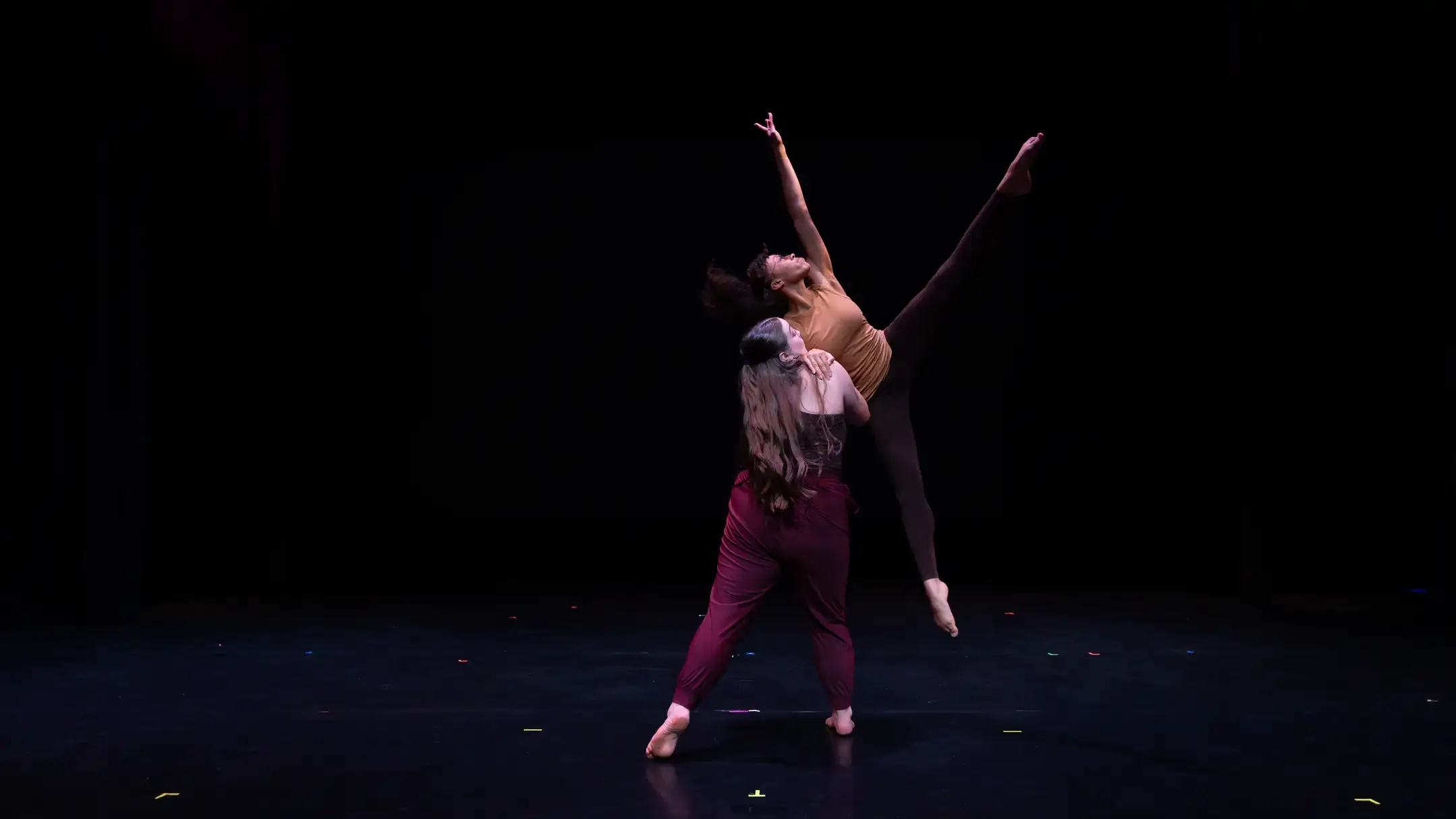 Two students dance on a dark stage