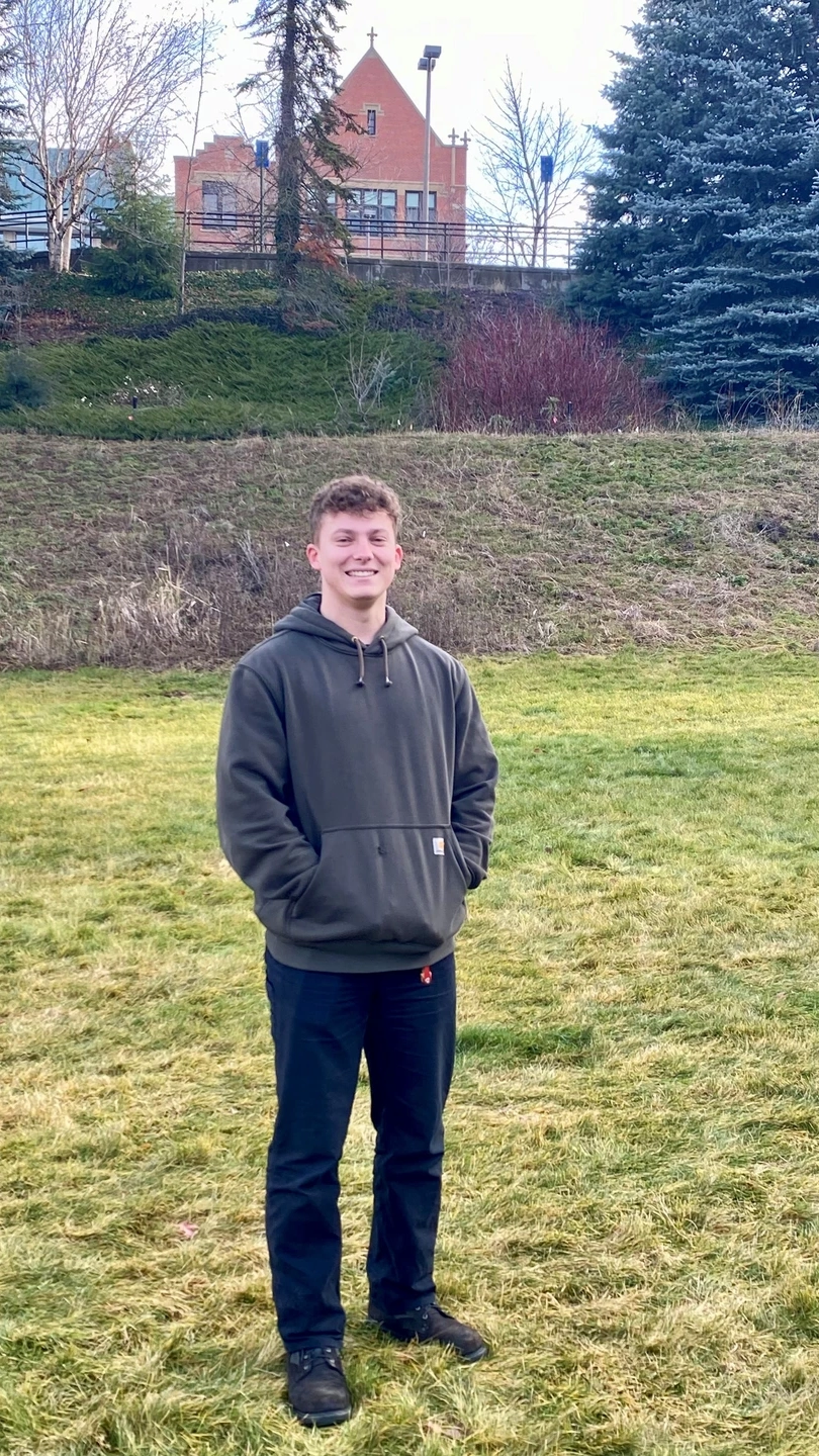 Man posing outside with trees in background. 