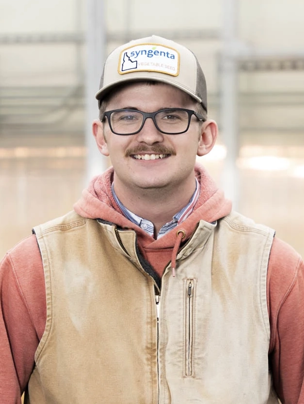 A man smiles with a greenhouse in the background.