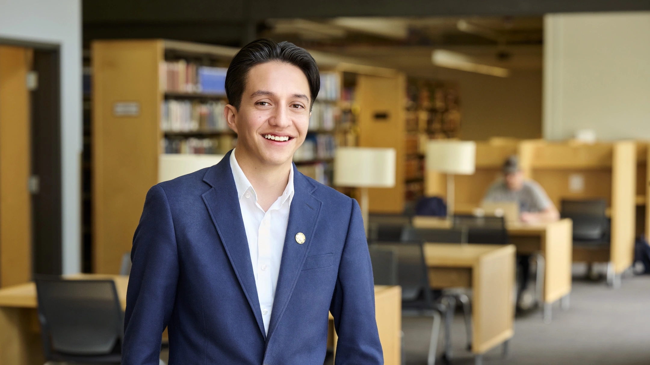 Student standing in a library looking at the camera smiling.