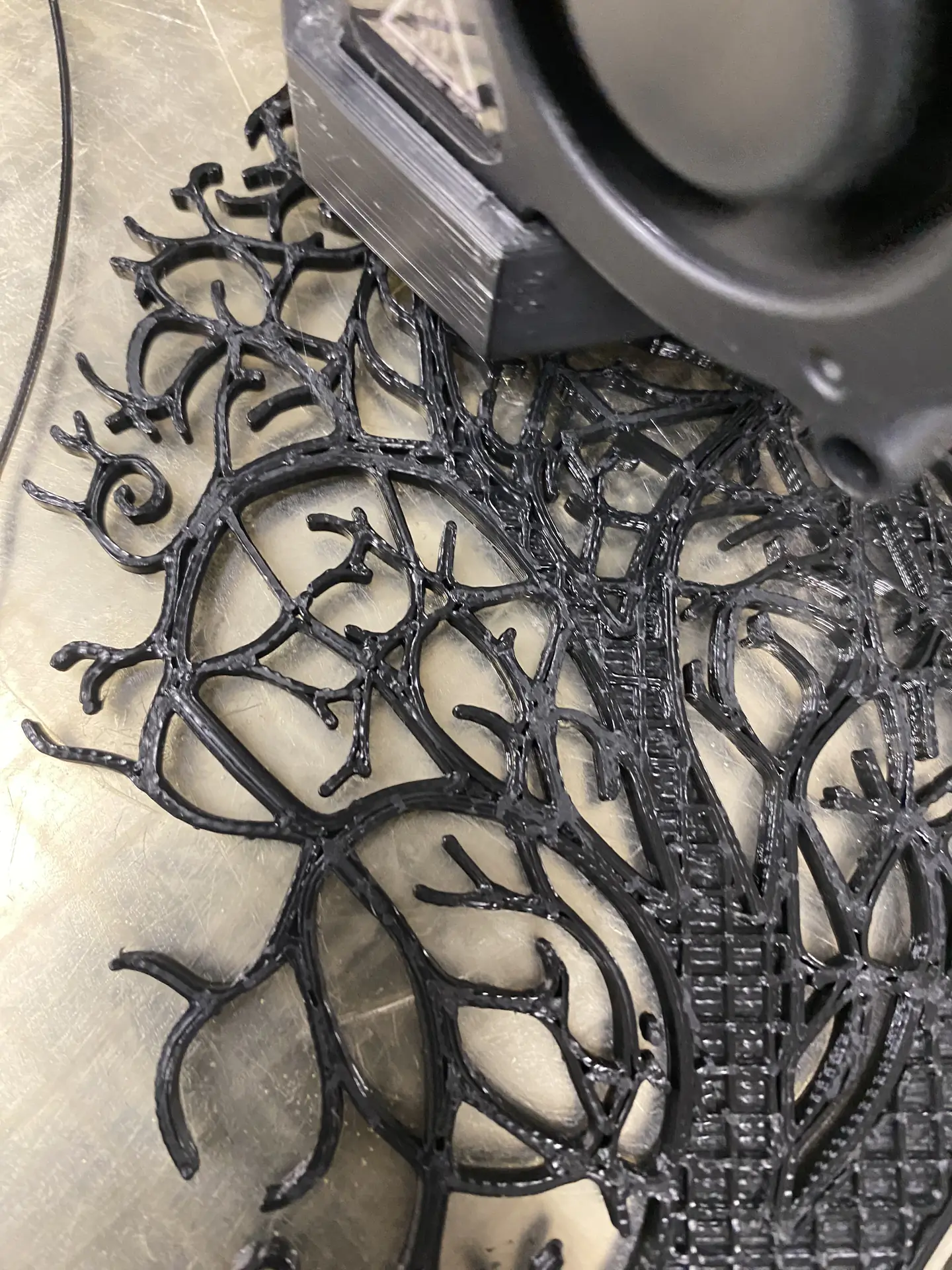 A close-up view of 3D-printed black, intricate branch-like patterns on a flat surface, showing detailed texture crafted by a printer.