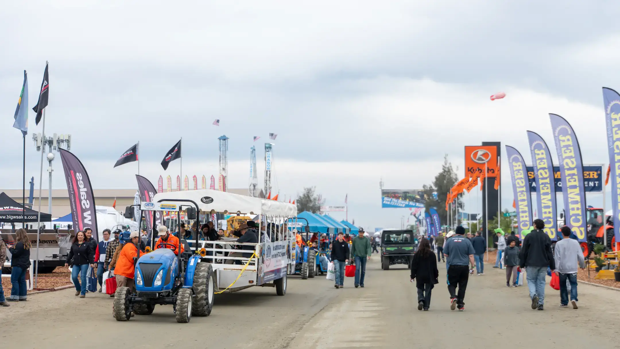The entrance of the World Ag Expo with banners and tractors and people walking.