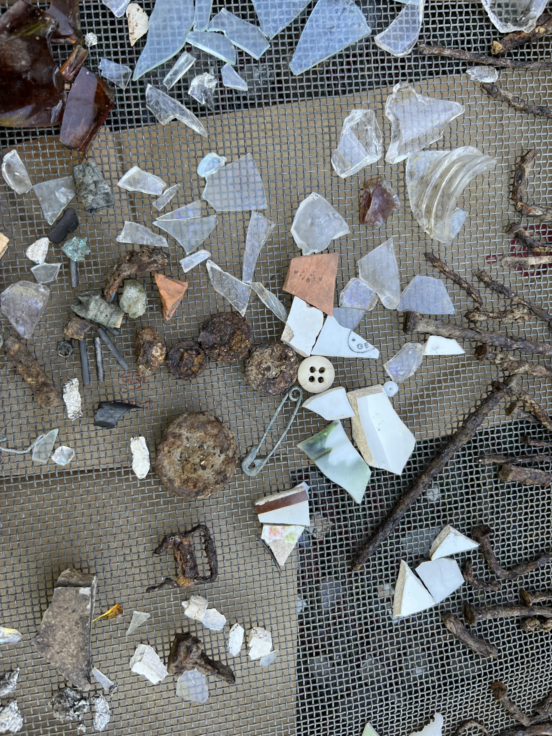 Glass fragments, shards of ceramics, rusted nails, buttons and more detritus on a sifting grate.