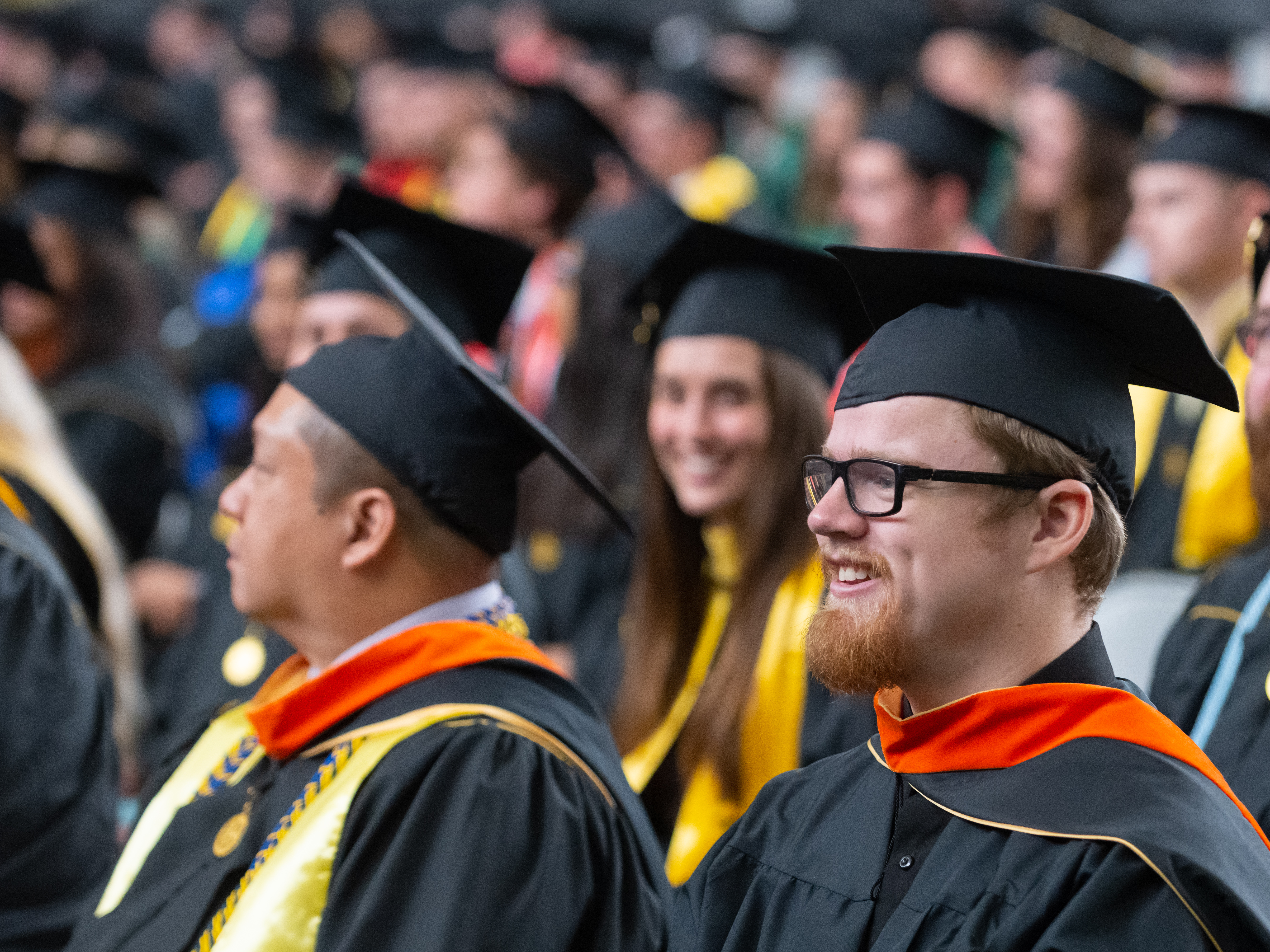 Man smiles while wearing graduation cap and gown.