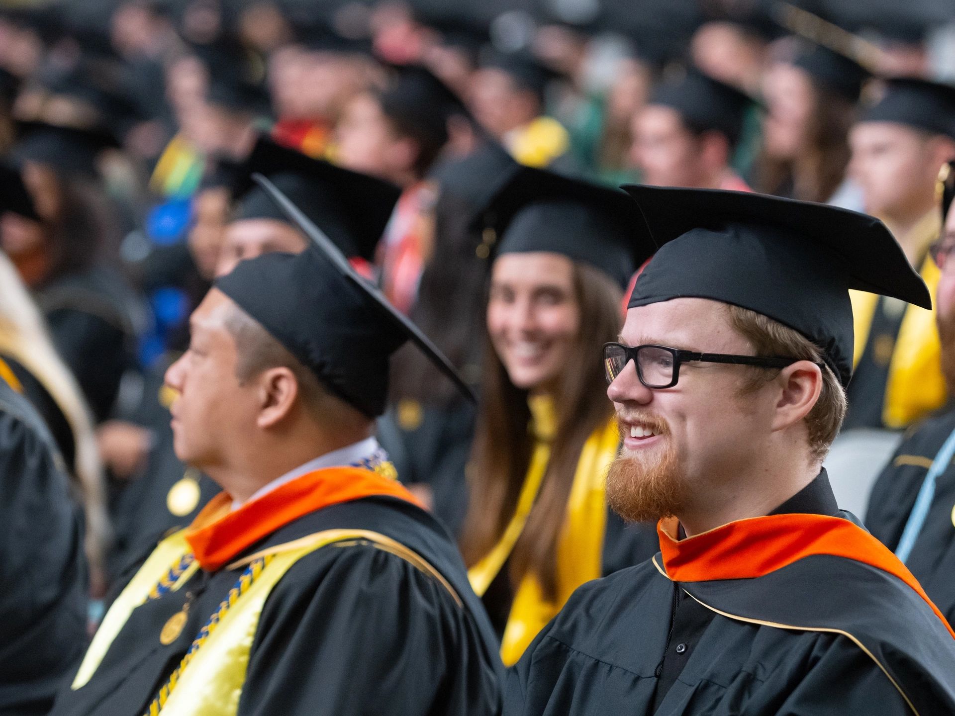 Man smiles while wearing graduation cap and gown.