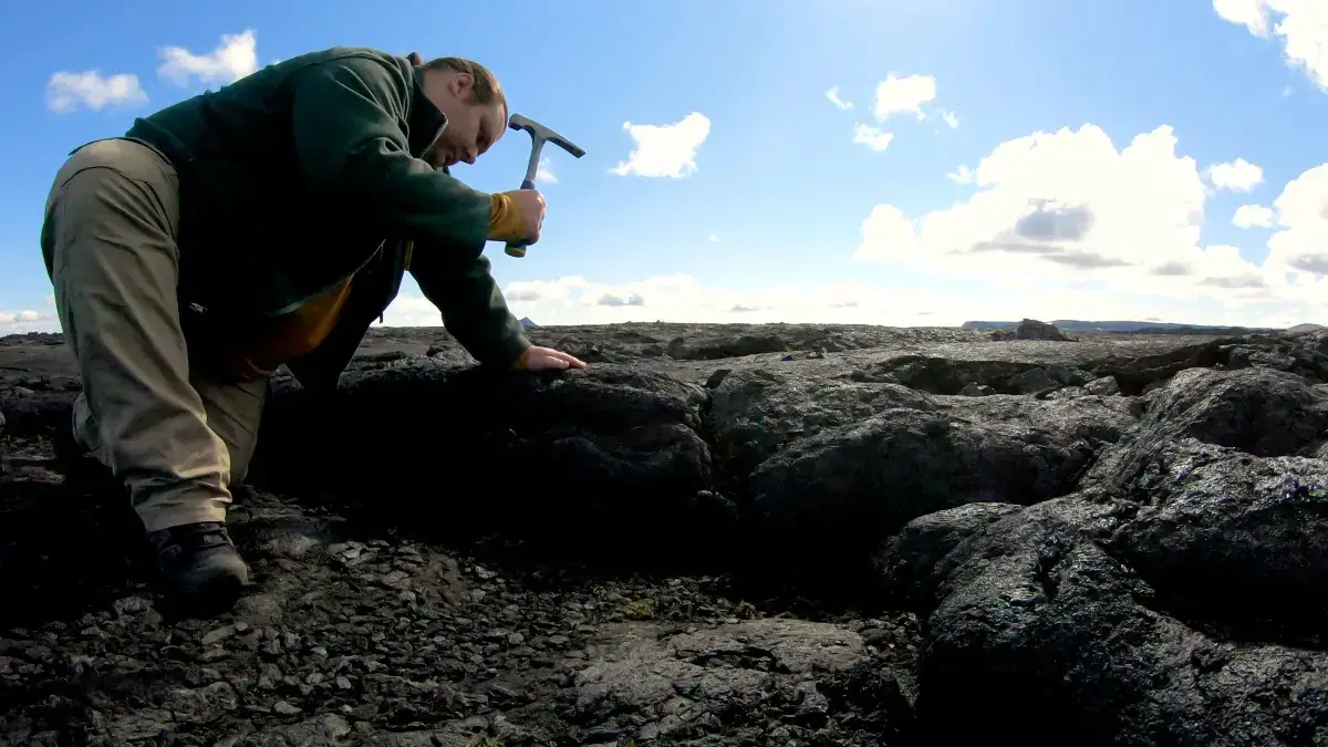 A man uses a hammer on black lava. 