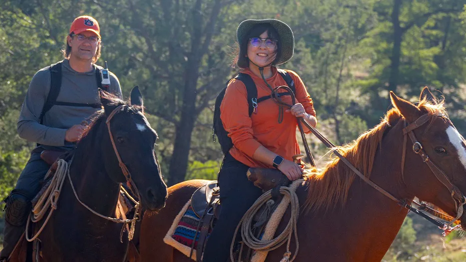 A man and woman riding horses in the woods.