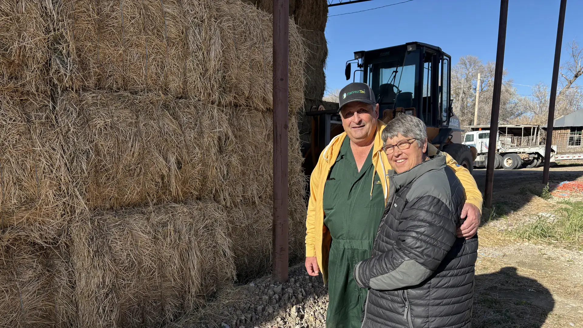 A man and his wife stand by a haystack.