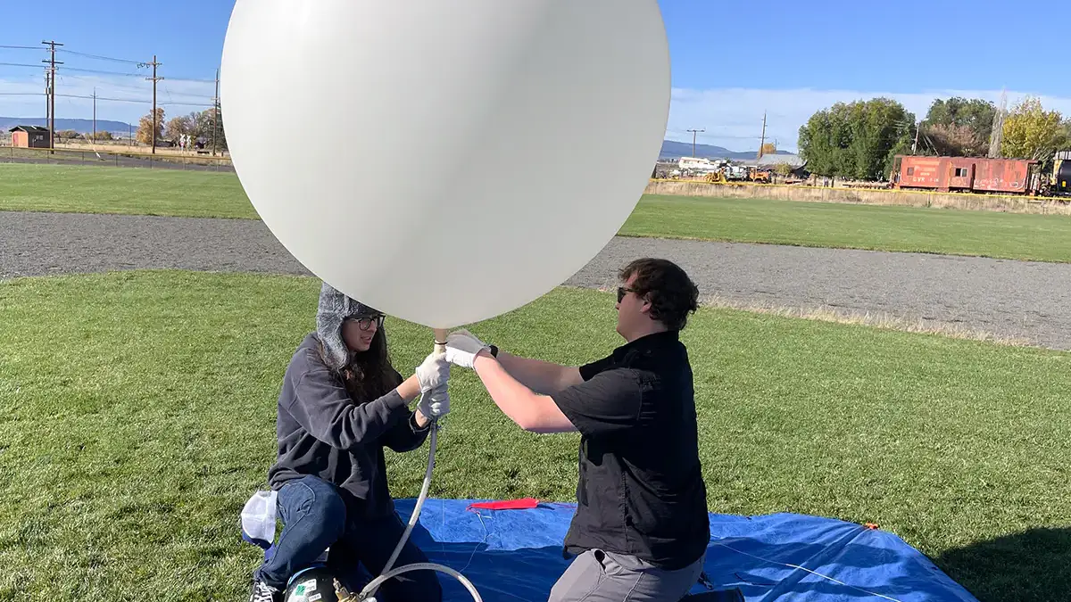 Two people fill a white weather balloon.