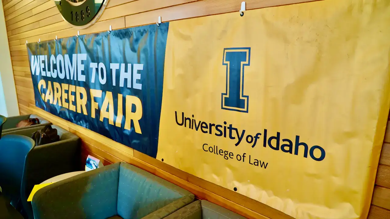 A banner in a room reads "Welcome to the Career Fair" in blue and yellow. Another banner displays "University of Idaho College of Law" with a large blue logo of the letter 'I'.