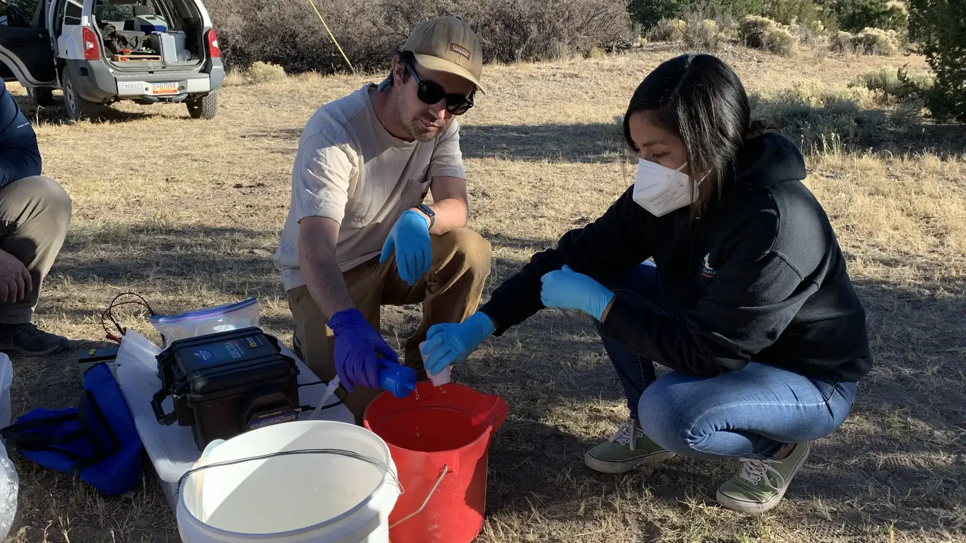 Man and woman poor water samples in a red bucket.
