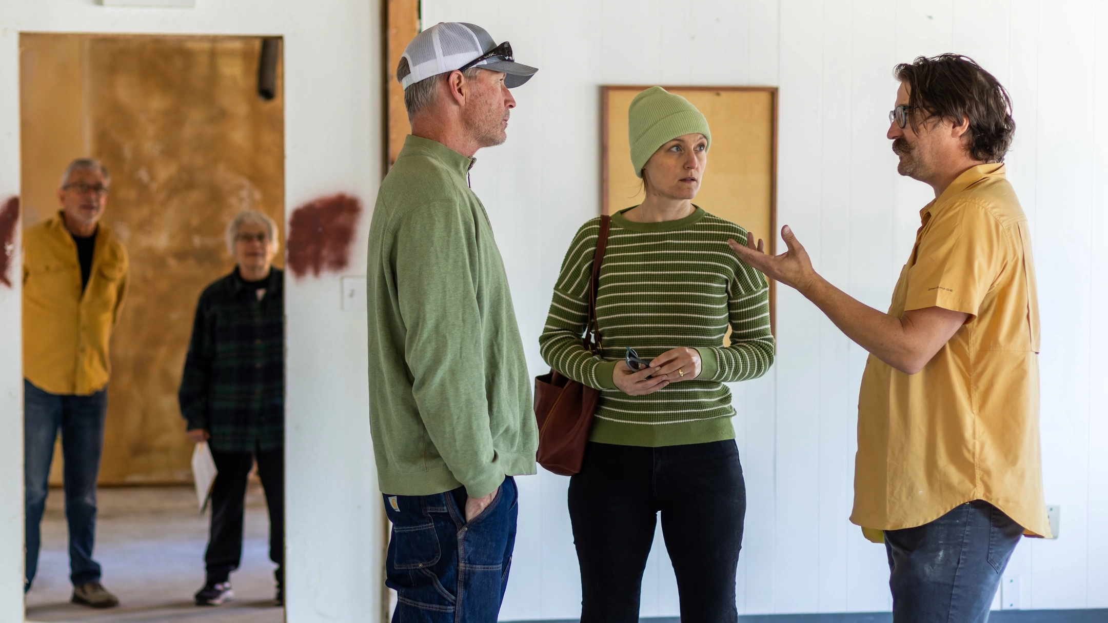 Man in yellow shirt speaking to man and woman wearing green