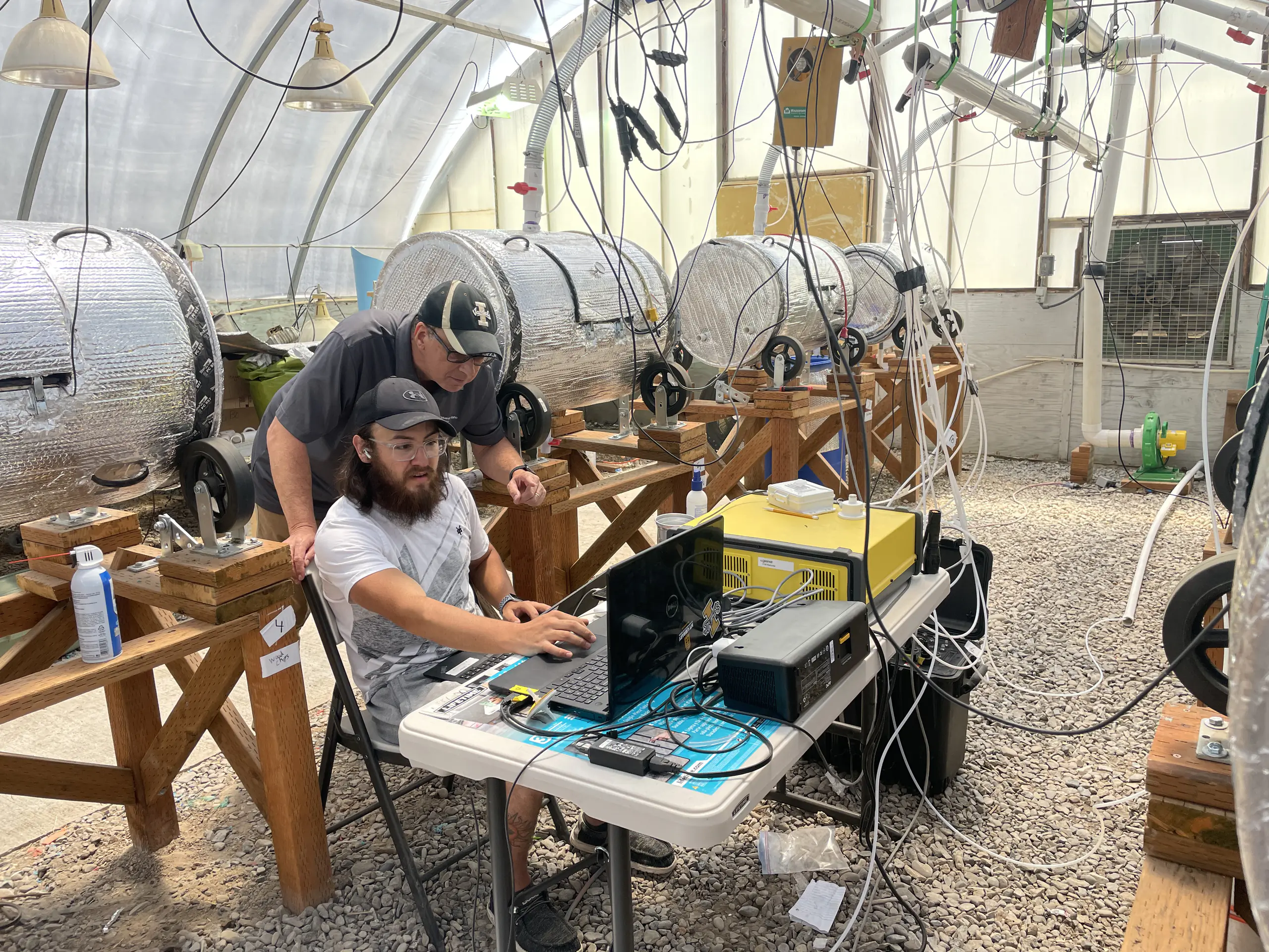 Two men work at a computer with foil bins behind them.