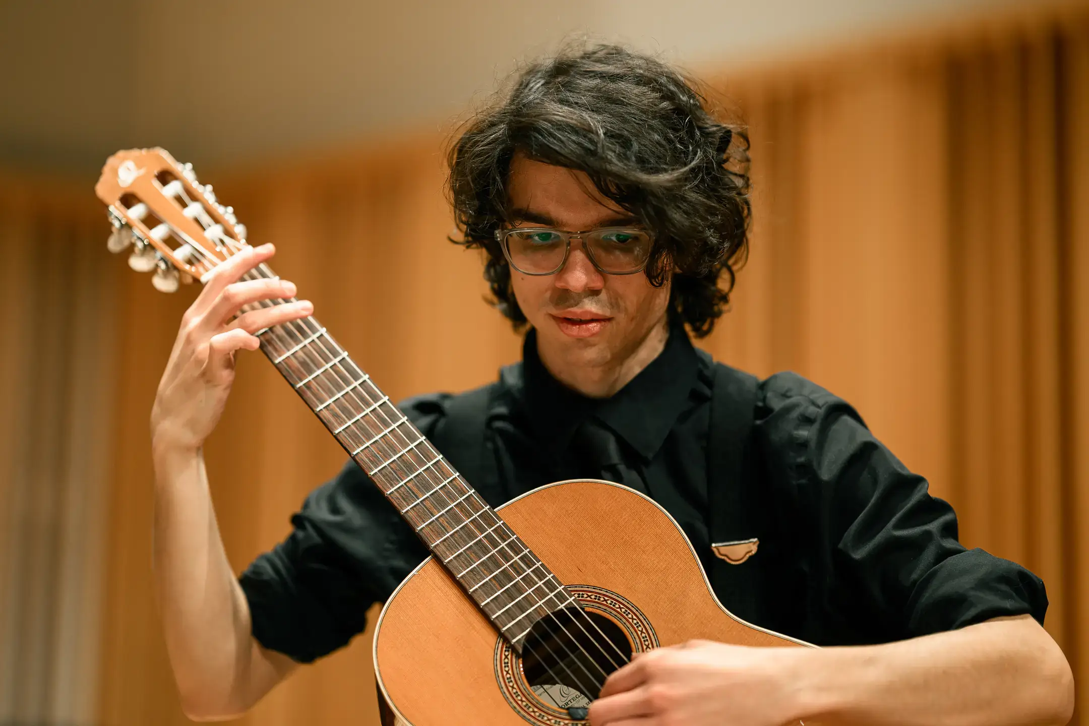 Young musician in black playing a classical guitar onstage, focused on the fretboard