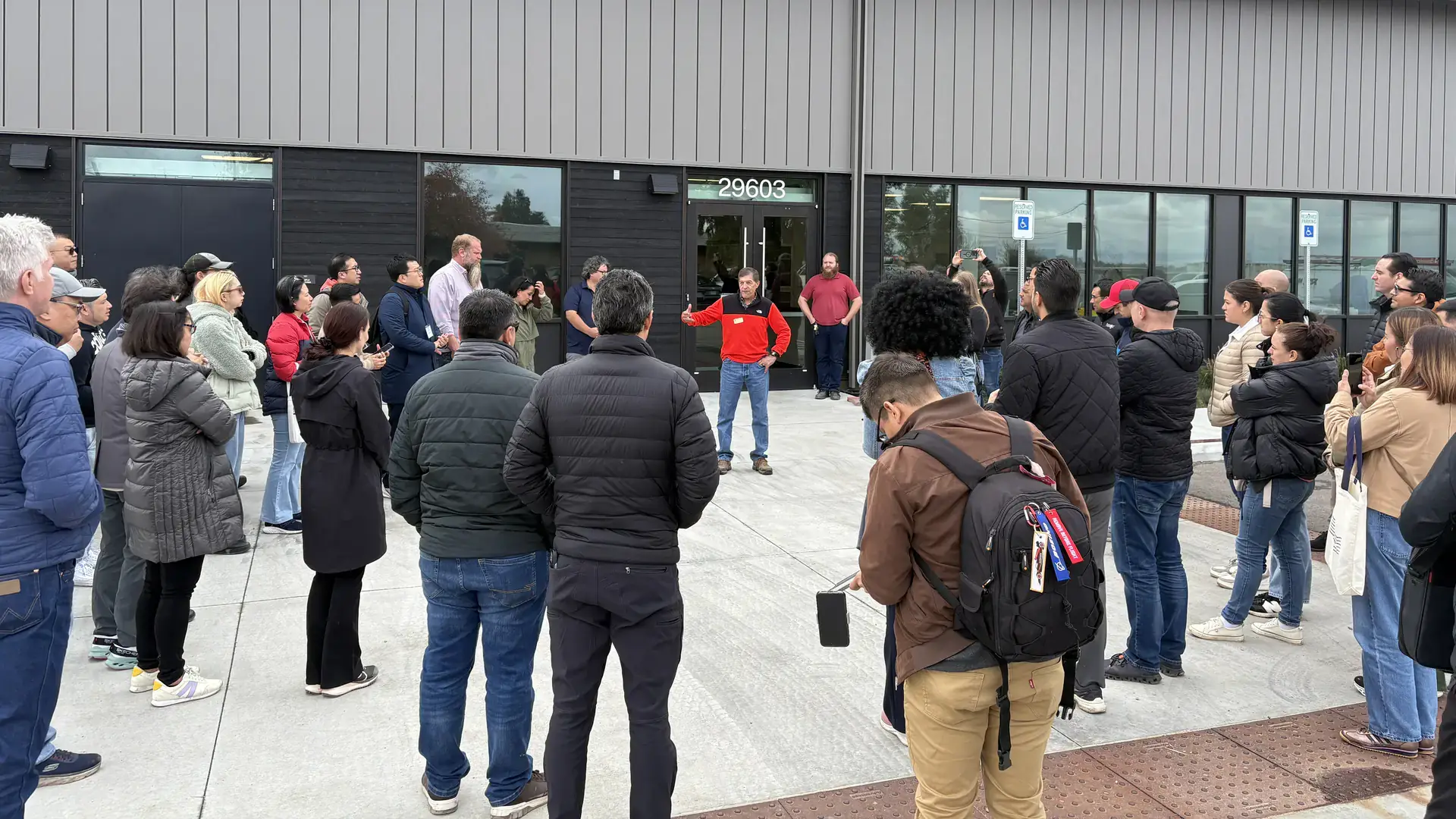 Chefs from foreign countries stand in a circle around a presenter in front of a long laboratory building.