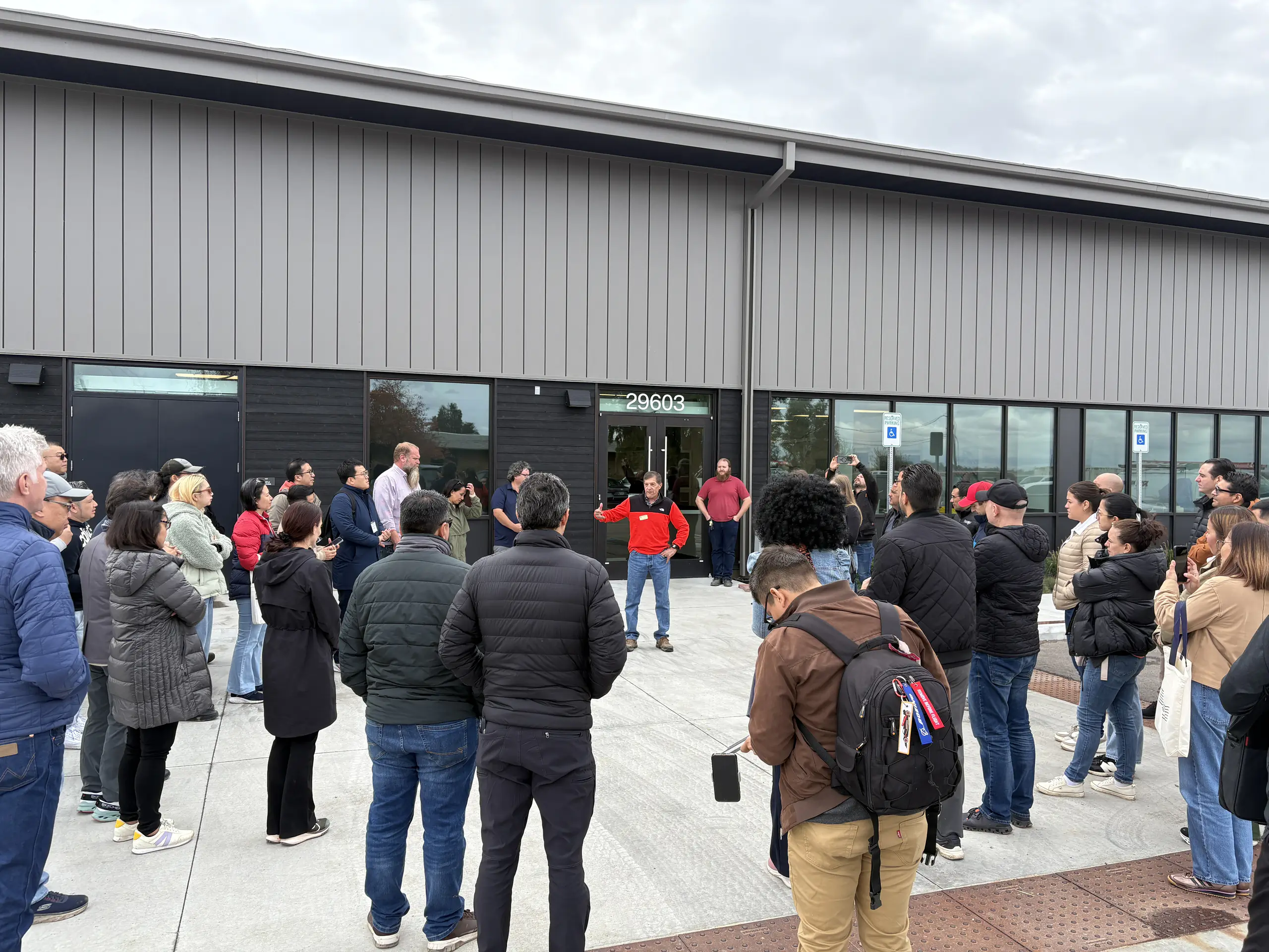 Chefs from foreign countries stand in a circle around a presenter in front of a long laboratory building.