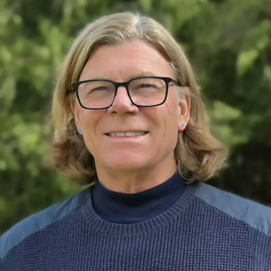 A portrait of a man with shoulder length hair and greenery in the background
