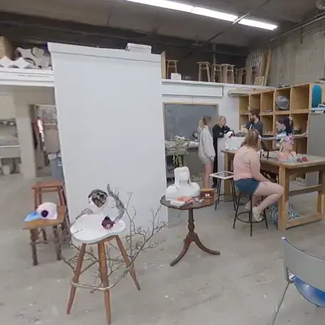 Students in room with cement walls and floors, sculptures on tables.