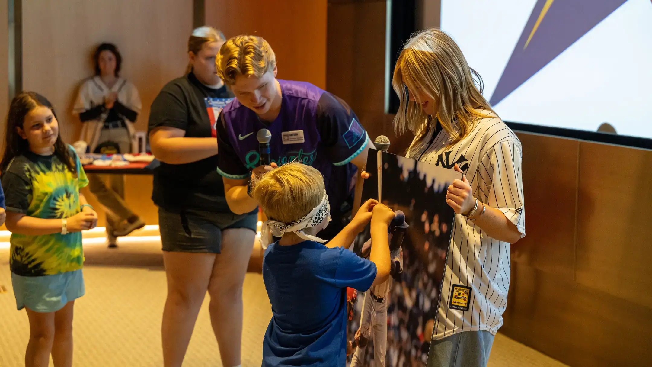 Woman holding a photo while blindfolded child is attempting to place a sticker on the photo.