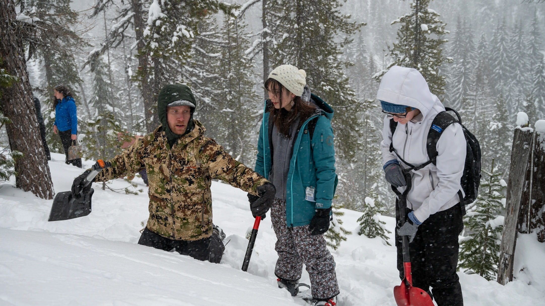 Man indicates with his arms while two students look on in snow field