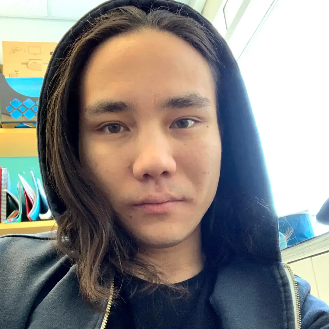 Headshot of a person with shoulder-length dark hair wearing a black hoodie indoors