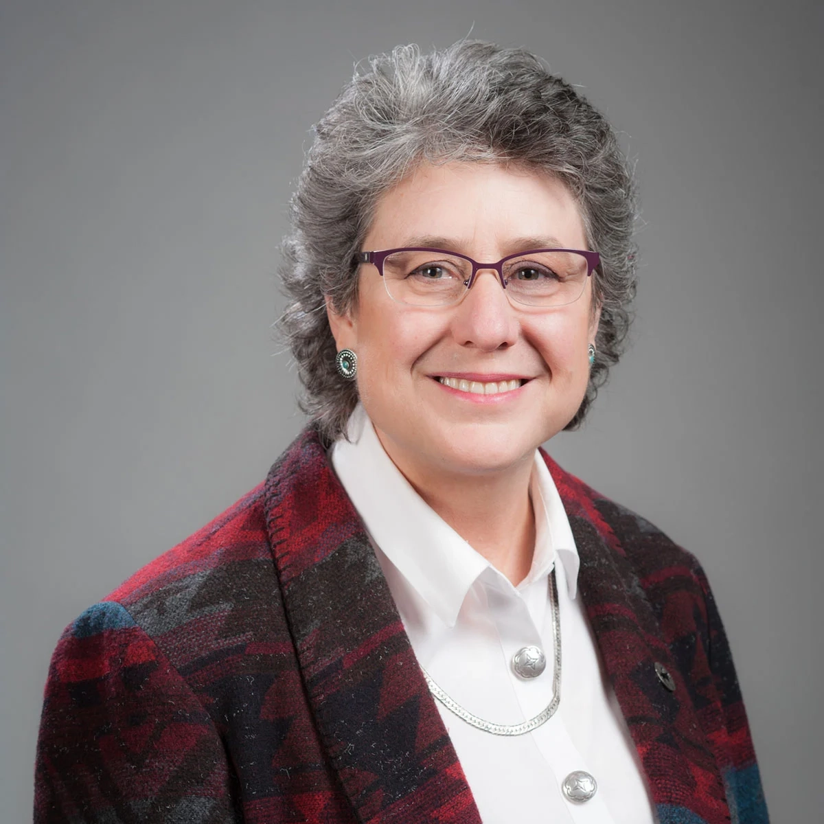 A professional portrait of a woman with grey hair and glasses
