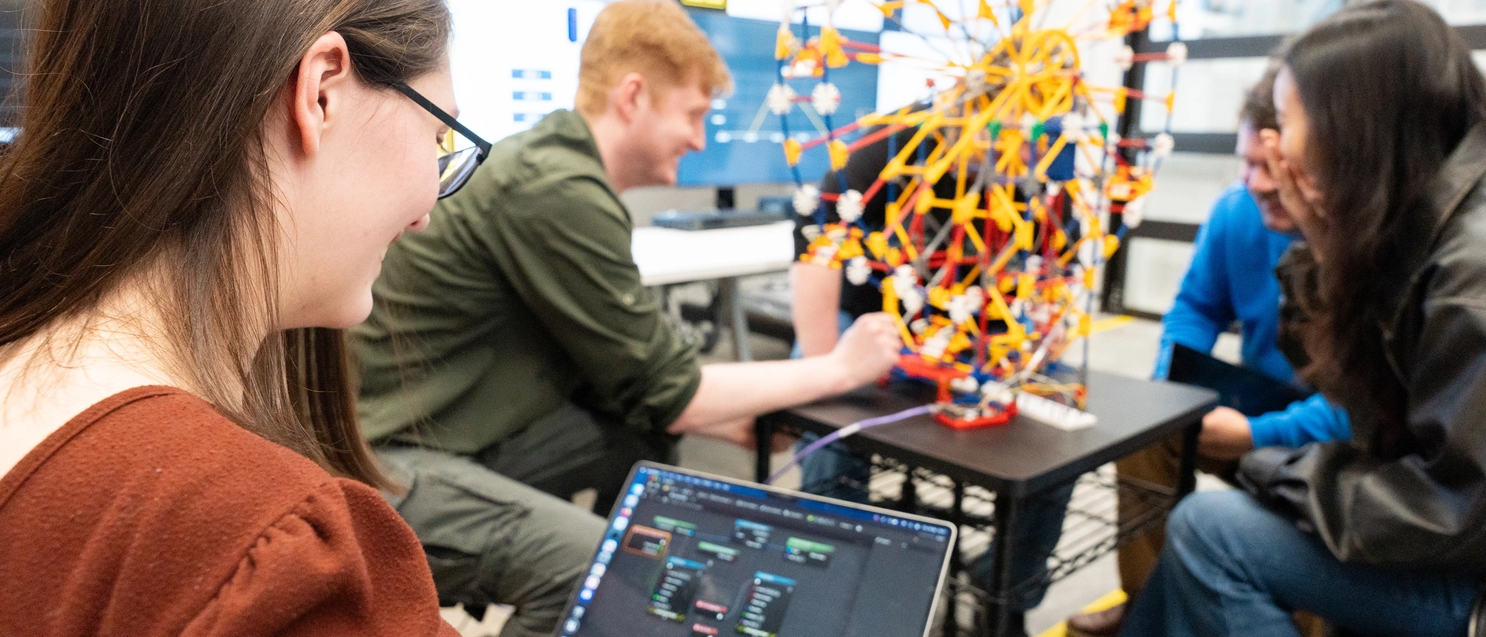 Photos of upcoming graduates in the cyber security program showing off a model ferris wheel which replicates how a cyber attack could affect mechanical processes.
