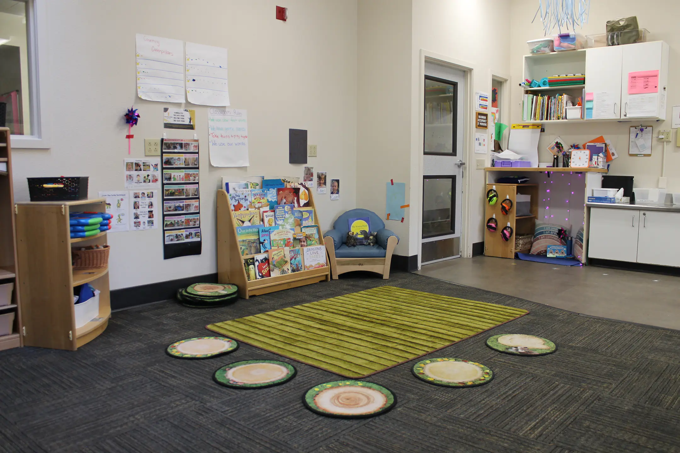 A classroom kitchenette and reading corner with chair, rug, and circular sitting rugs.