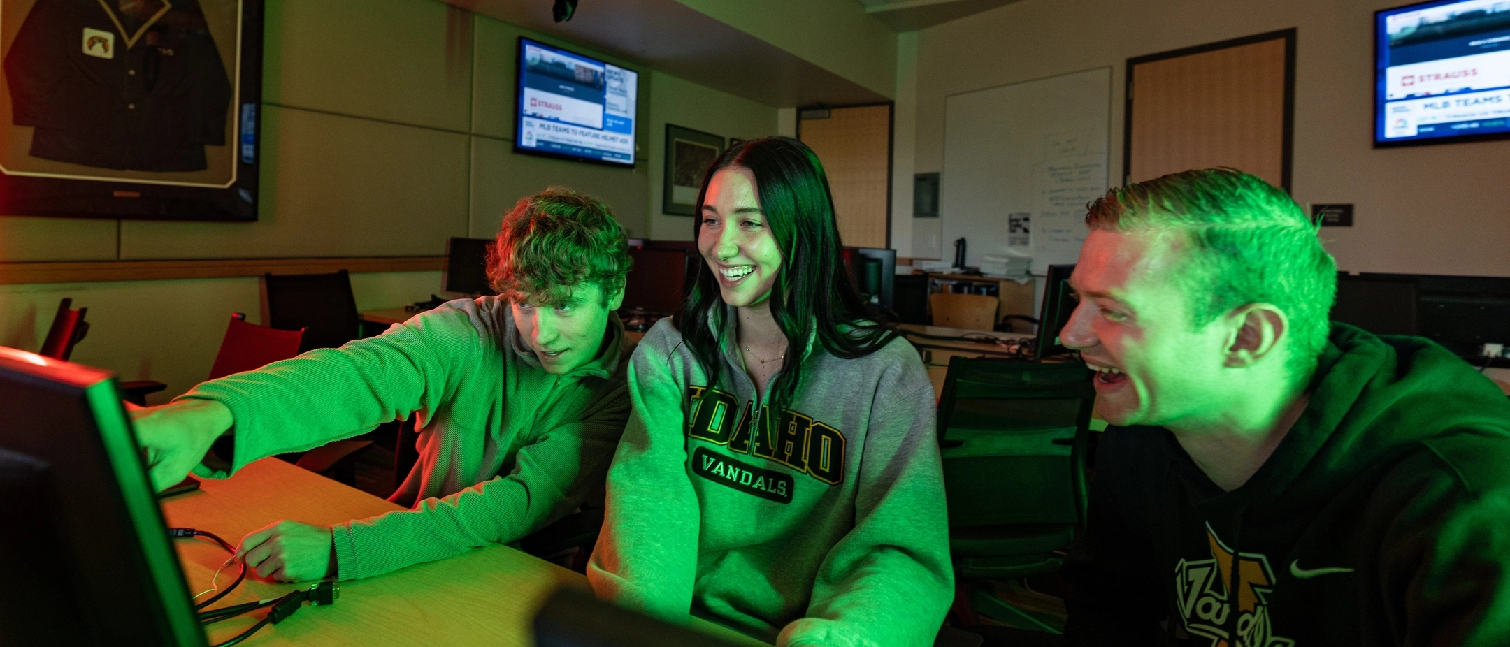 Three U of I students looking at financial data on a computer screen in a classroom. 