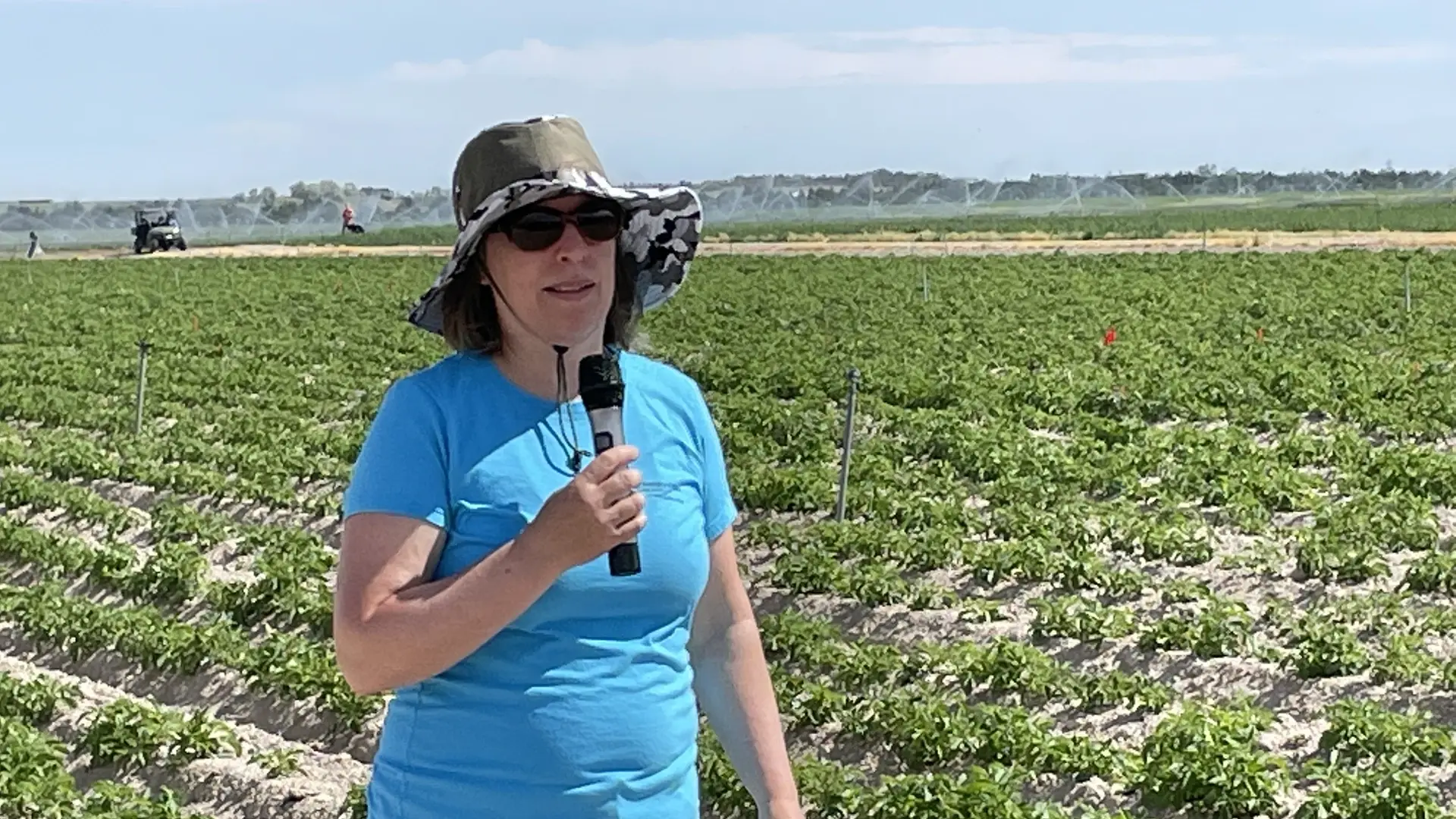 Kasia Duellman stands holding a microphone in a potato field.