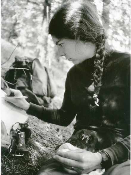 A woman holds an owl in her lab and takes notes