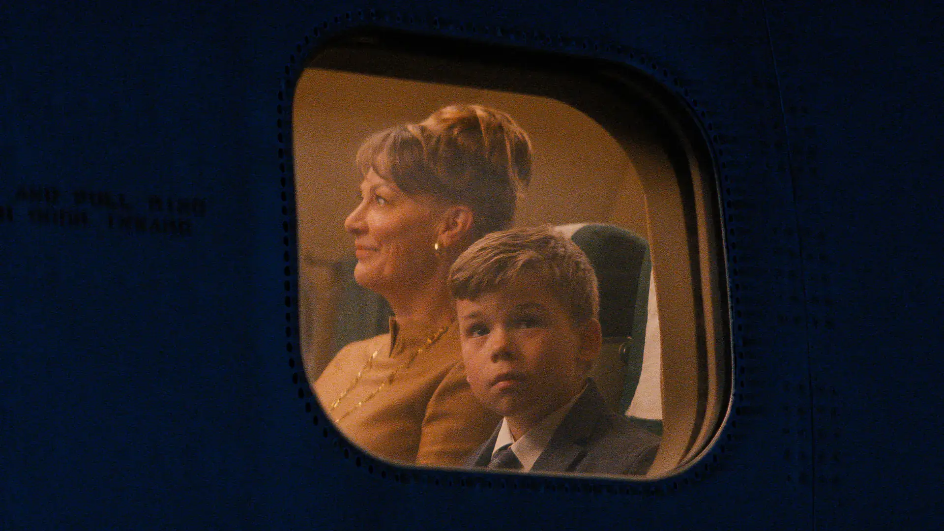  woman and a young boy are pictured through an airplane window.