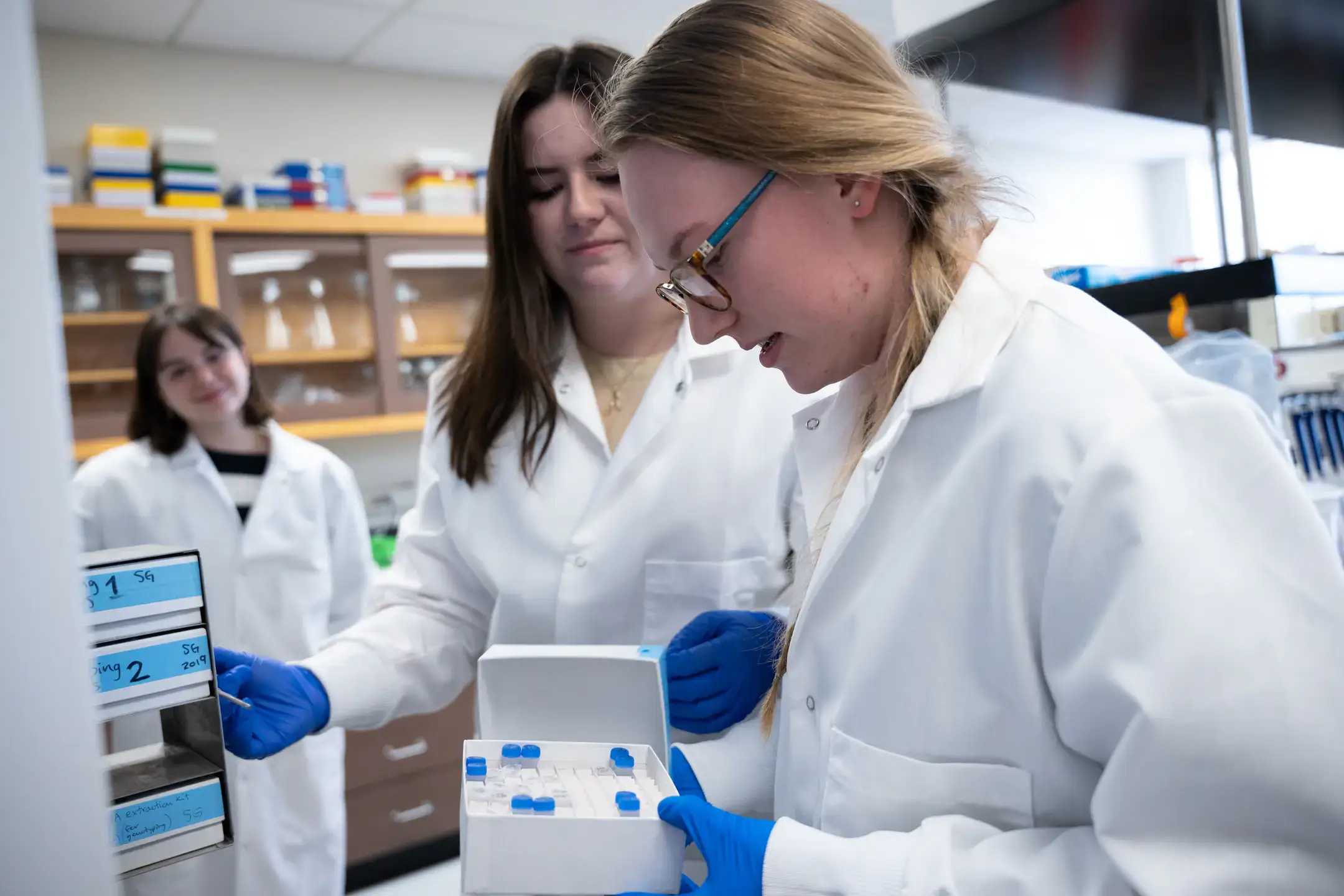Students wearing white lab coats work with test tubes in a laboratory..