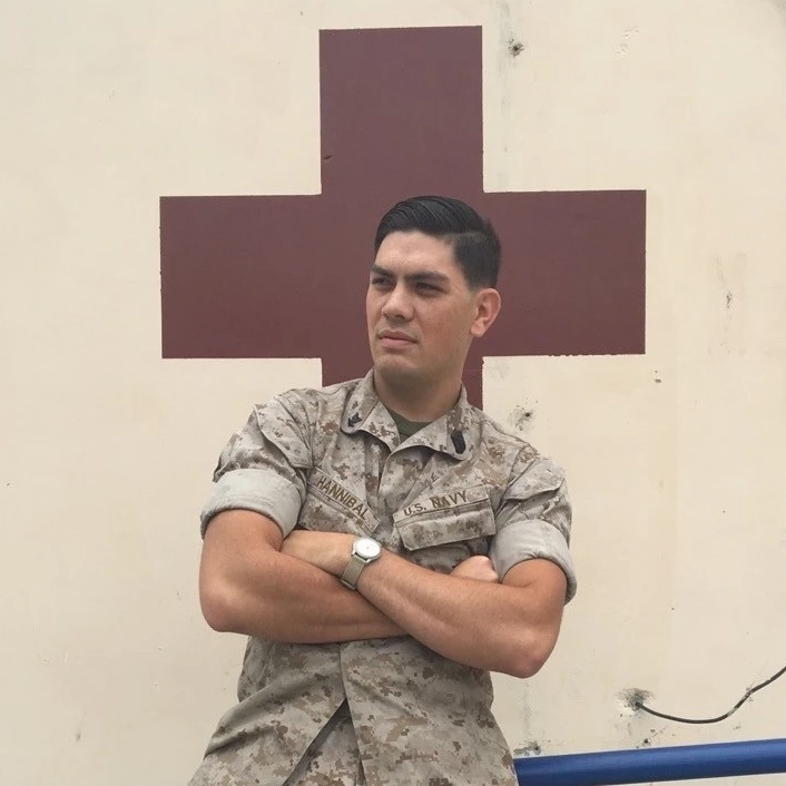 Man in military fatigues standing in front of a red cross