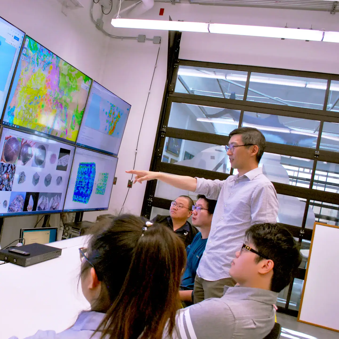 A man teaches students in front of screens.
