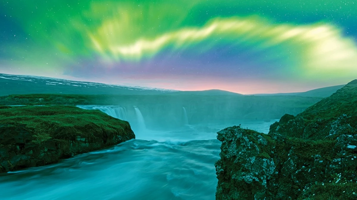 The northern lights shining over waterfalls in Iceland.