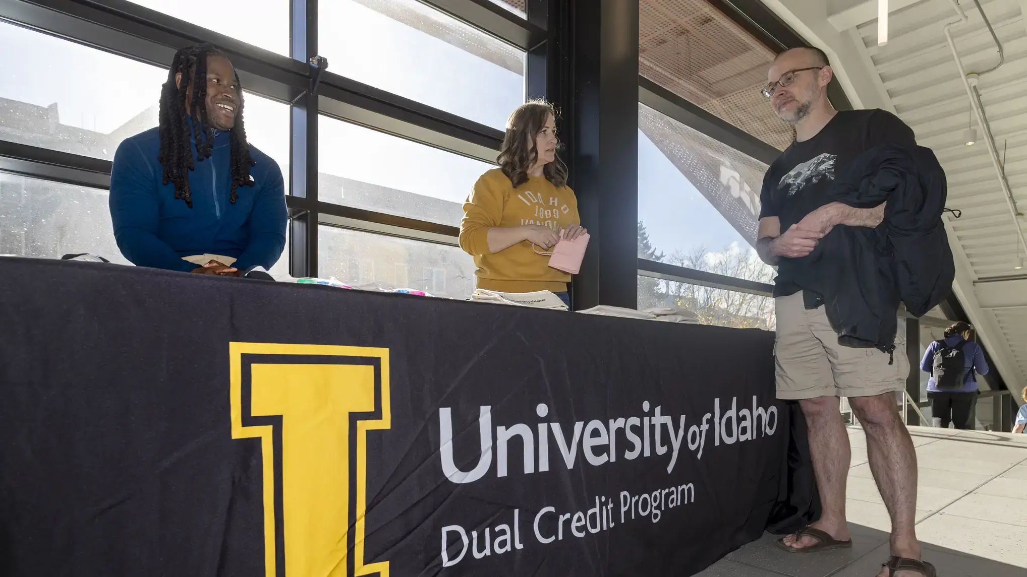 Lorenzo Rene and another person at a table for the U of I Dual Credit Program, talking to a student.